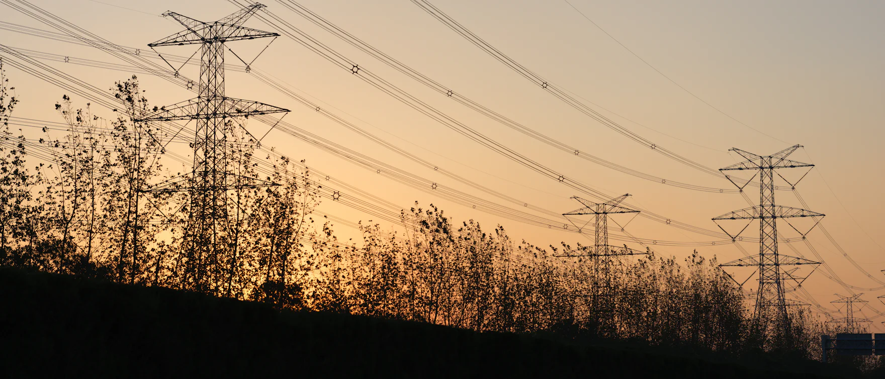 Transmission towers and power lines silhouetted against the sky at dusk, receding into the distance.
