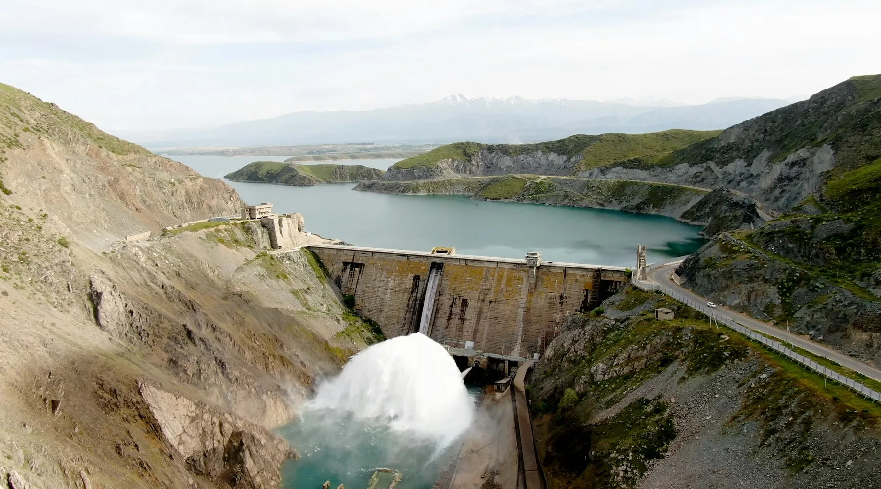 Hydroelectric dam releasing water into a valley between mountains.